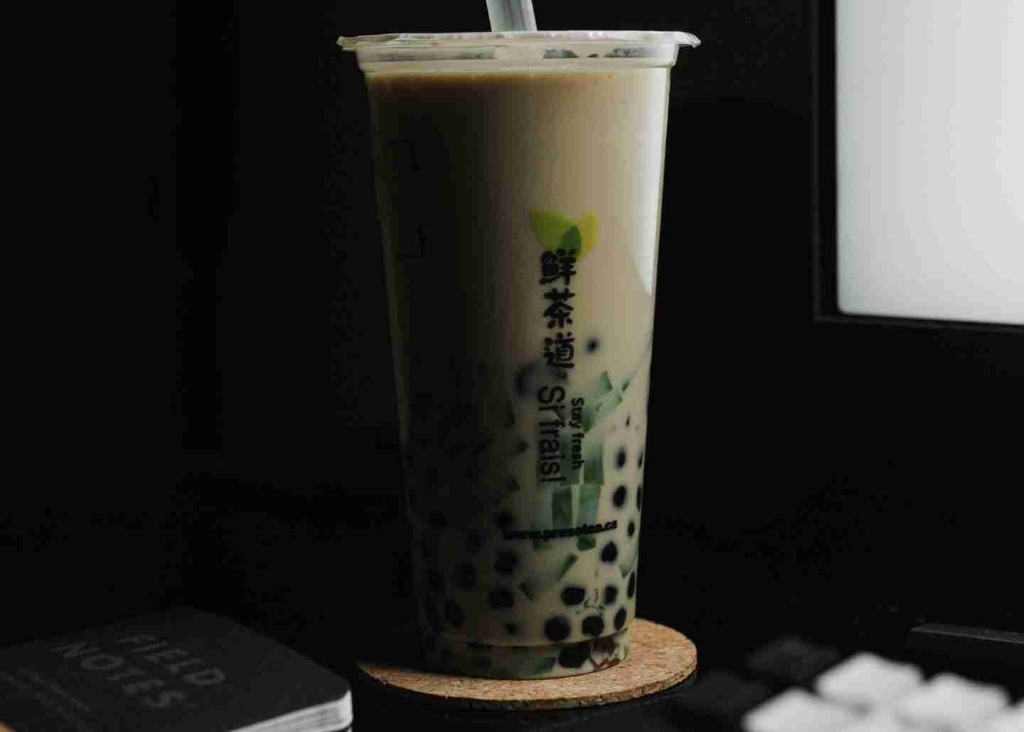 Bubble tea resting on a coster between a computer and a notebook.