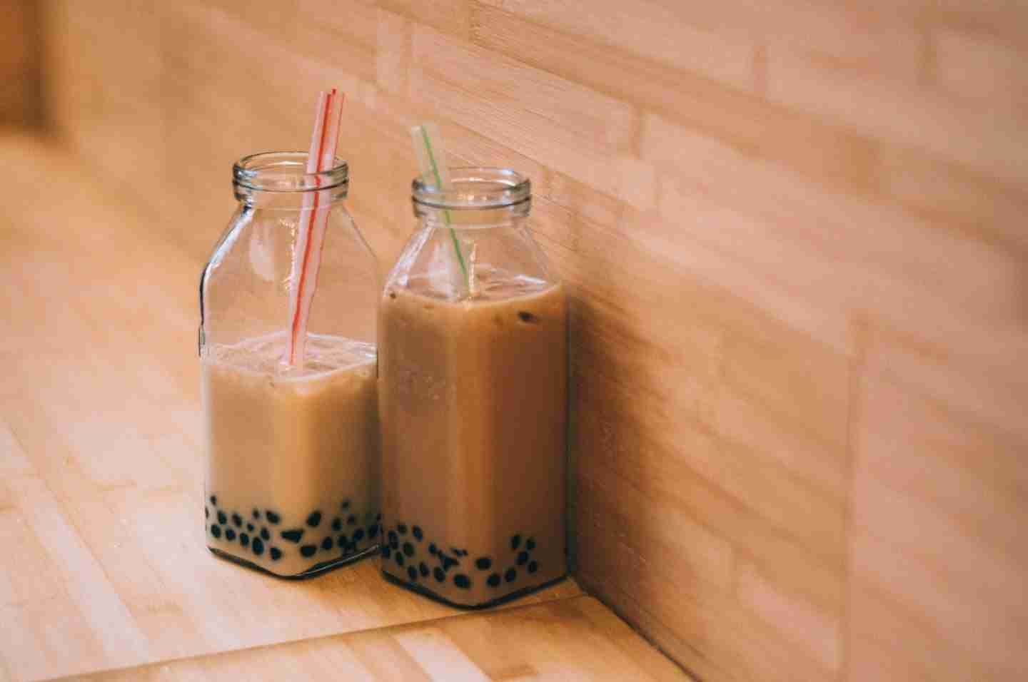 Two glass jars with bubble tea and straws inside them.