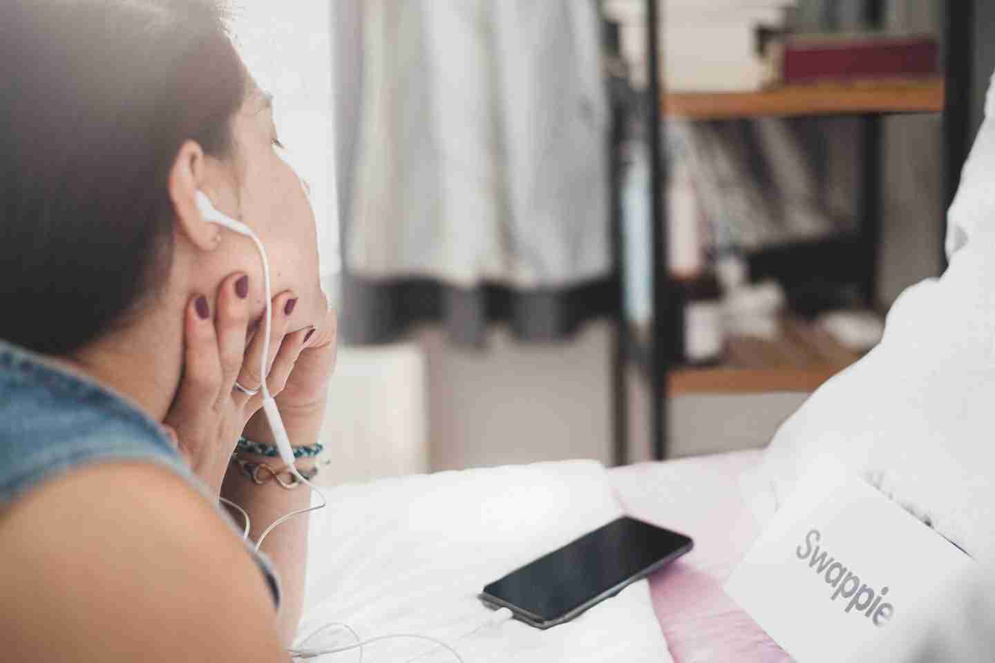 woman in white tank top holding white earbuds listening to podcasts