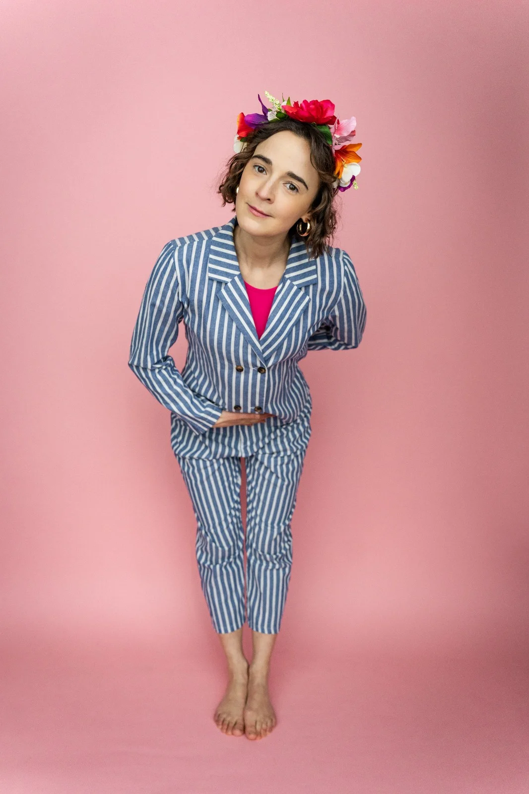 Philippa Dawson in a blue and white pinstripe suit with flowers in her hair on a pink background