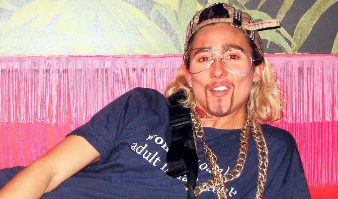 drag king wearing cap and gold chain.