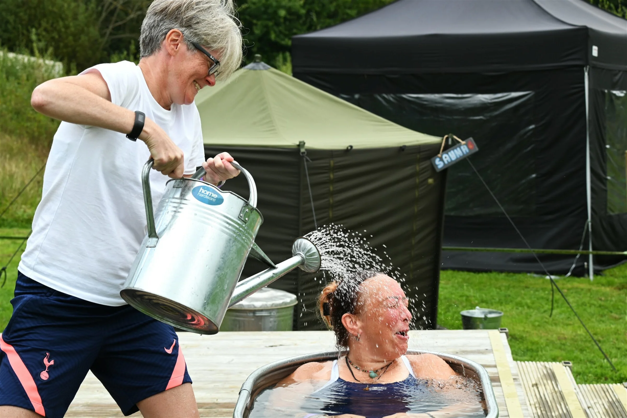 Guest at this year's wellness event sitting in ice bath, with another guest pouring a bucket of water on her.