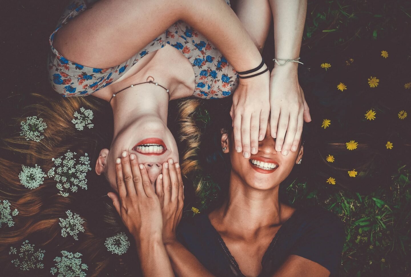 two women smiling while laying on lawn field