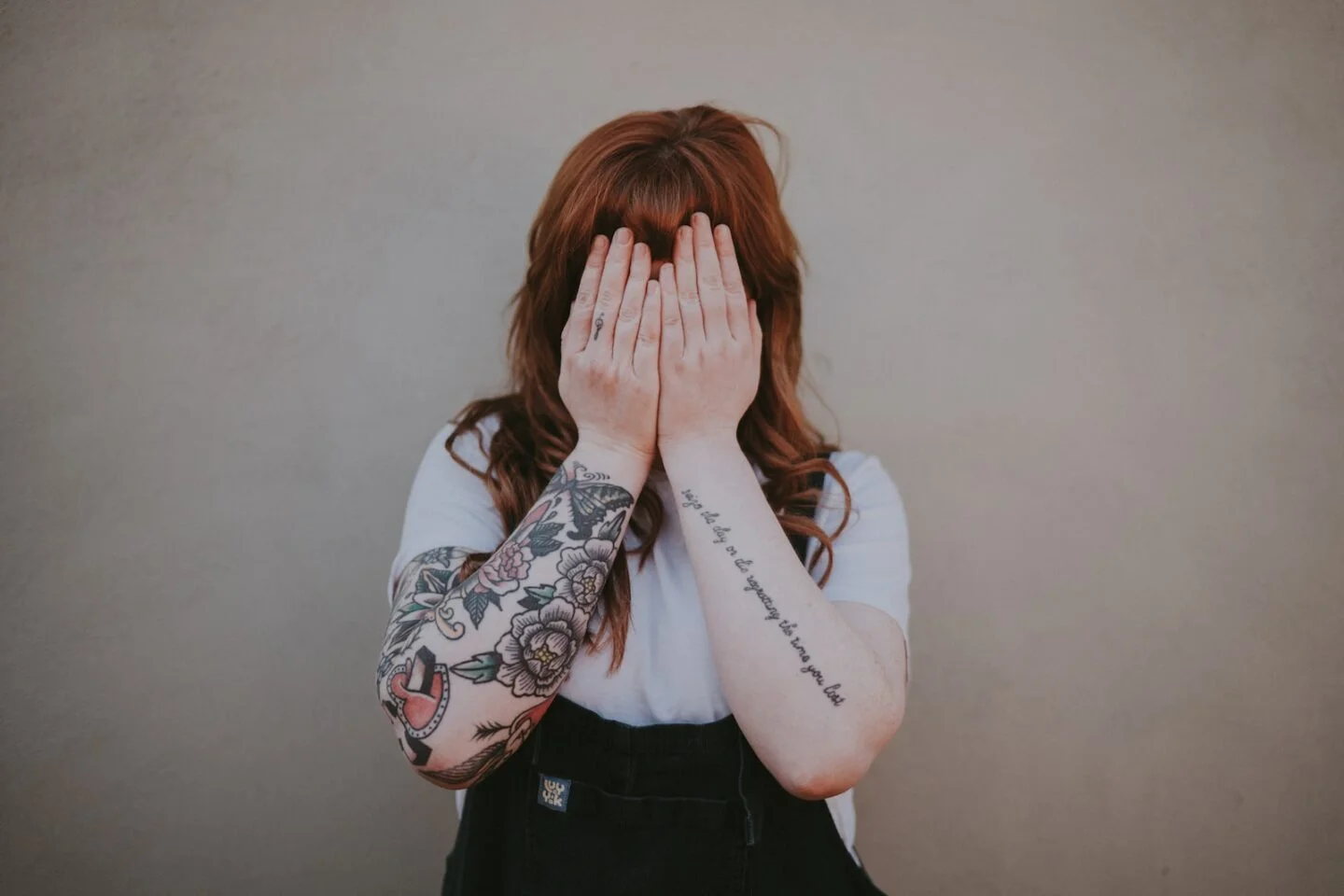 woman covering her face in front of wall with tattoos